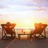 Two individuals reclining on lounge chairs at the beach during a glowing sunset, highlighting the calm that comes from safeguarding your family fortune across generations.