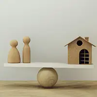 Wooden people figures and a small house balanced on a seesaw, symbolizing the delicate balance and control needed to manage family assets and secure family property