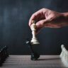 Businessman's hand captures black king with white queen on chessboard, symbolizing strategic decision-making and smarter financial moves using structured intelligence beyond instincts