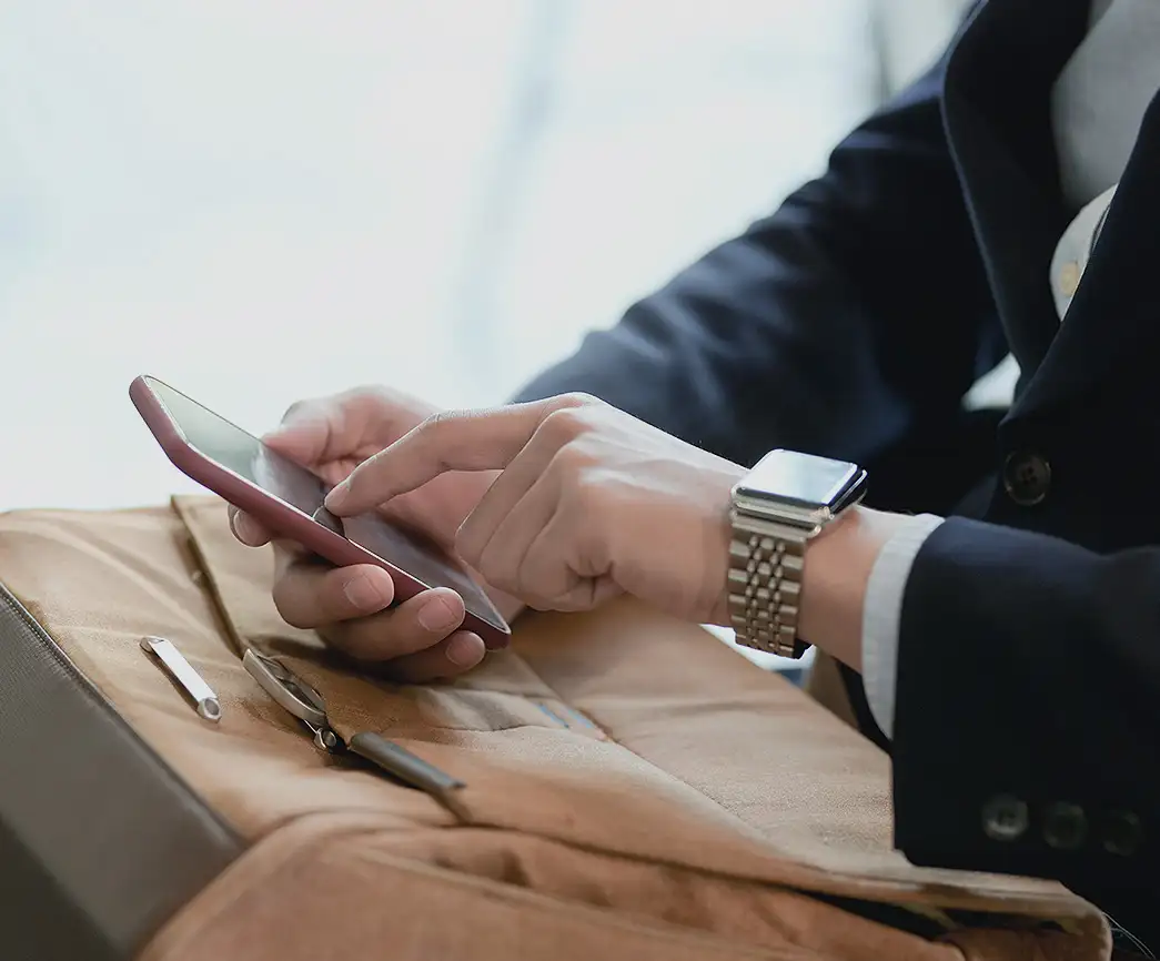 Close-up of a person in a suit and watch using a smartphone, suggesting professional engagement and modern financial management. The scene highlights AV's platform for UHNW client relationships.