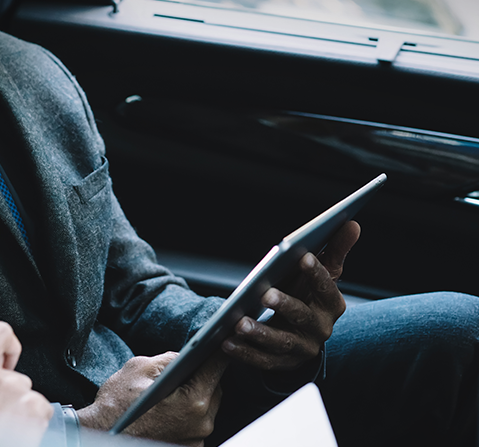 A business professional holding a tablet while seated in a car, reflecting the convenience and mobility of managing wealth through advanced technology, showcasing Asset Vantage’s modern financial solutions