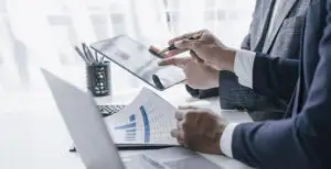 A professional businessperson uses a tablet to analyze financial data while reviewing printed charts and graphs. Streamlining compliance and unifying data for improved efficiency in family office operations.